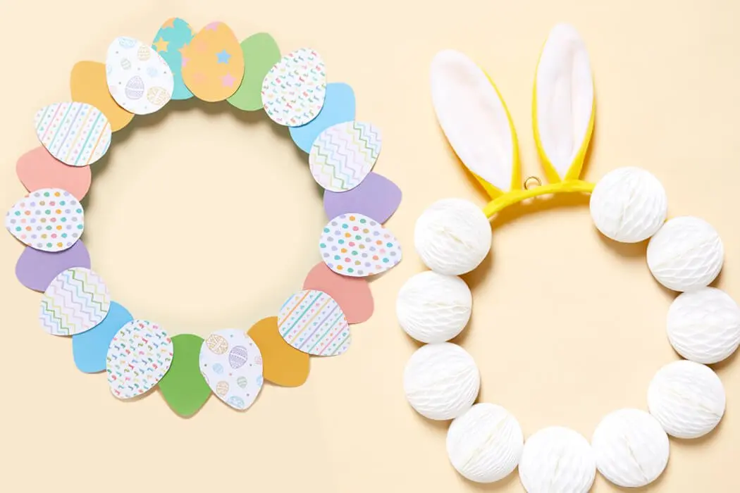 Two Easter Wreath decorations placed side by side, one with coloured paper eggs and the other with bunny ears and pom poms