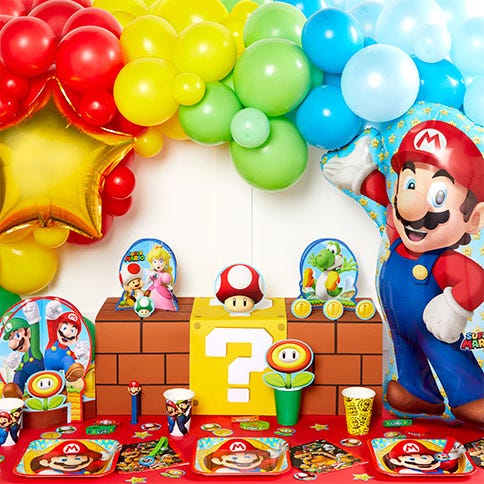 the picture shows Super Mario party decorations, including a red, yellow, green and blue balloon arch, a giant Mario balloon, Mario boxes and table decorations, as well as paper plates, cups and napkins.